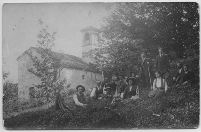Gruppo di persone sedute in posa accanto alla chiesa di San Clemente nei boschi di Vaglio