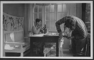 Mario Bernasconi prepara una cornice mentre Irma è seduta al tavolo