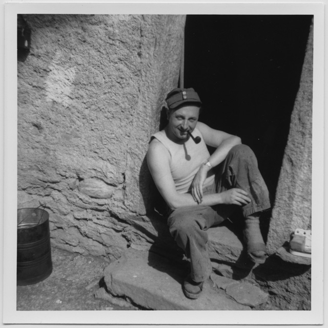 Uomo seduto sulla soglia di una casa con pipa