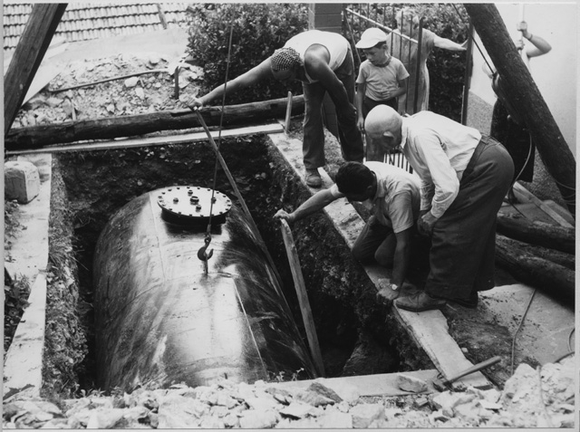 Uomini al lavoro durante la posa di una cisterna a Roveredo