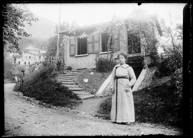 Donna in posa davanti ad un abitazione a (?)