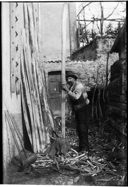 Ritratto di uomo mentre scorteccia dei pali con un falcetto